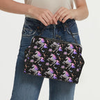 Model carrying kisslock bag with skeleton unicorns with purple and pink manes on black by the top handle