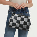Model carrying kisslock bag with black and white checkerboard pattern by the top handle